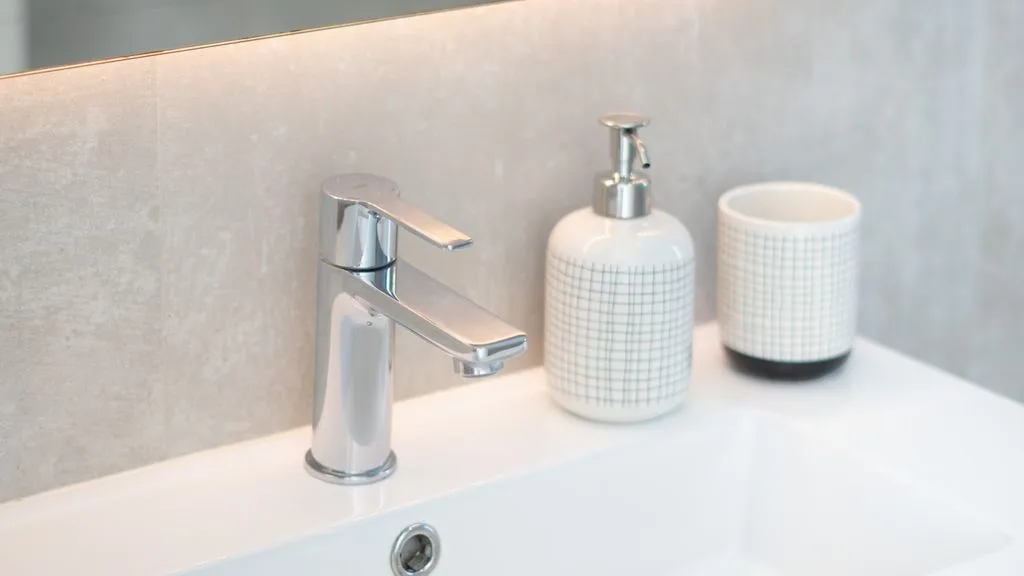 A bathroom sink with a chrome faucet and countertop containers.
