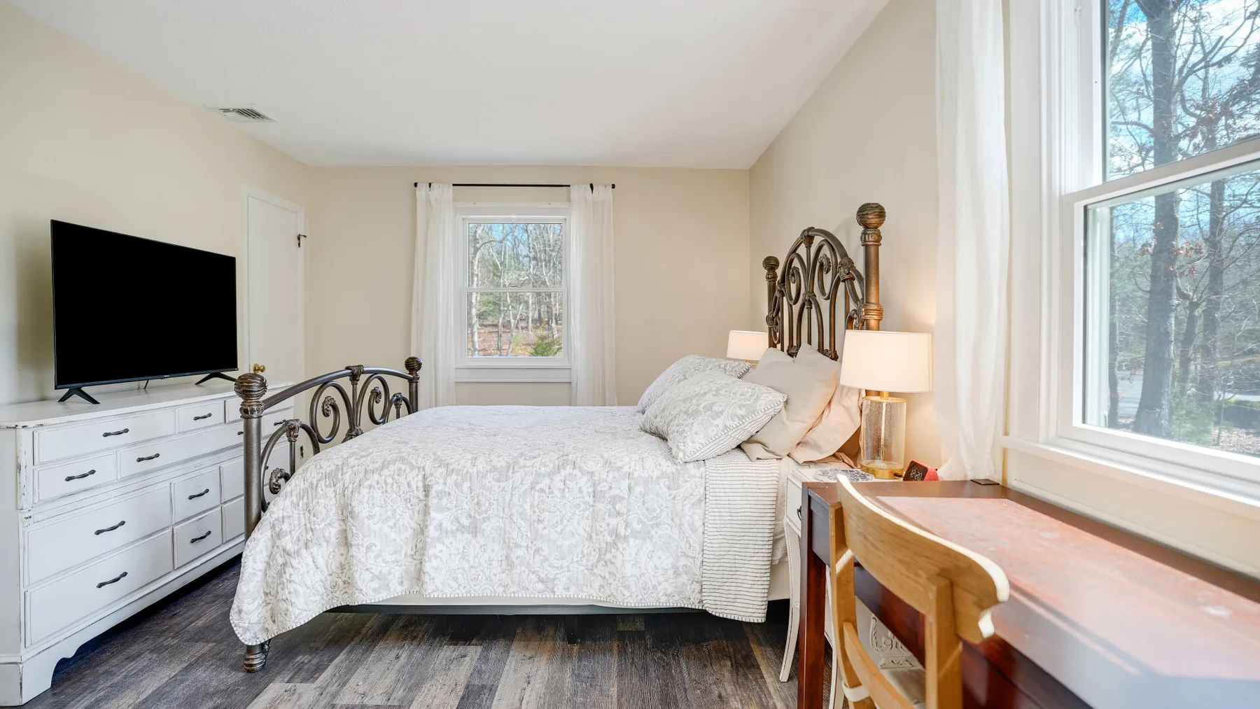 A bedroom with a bed, dresser, and large windows overlooking trees.
