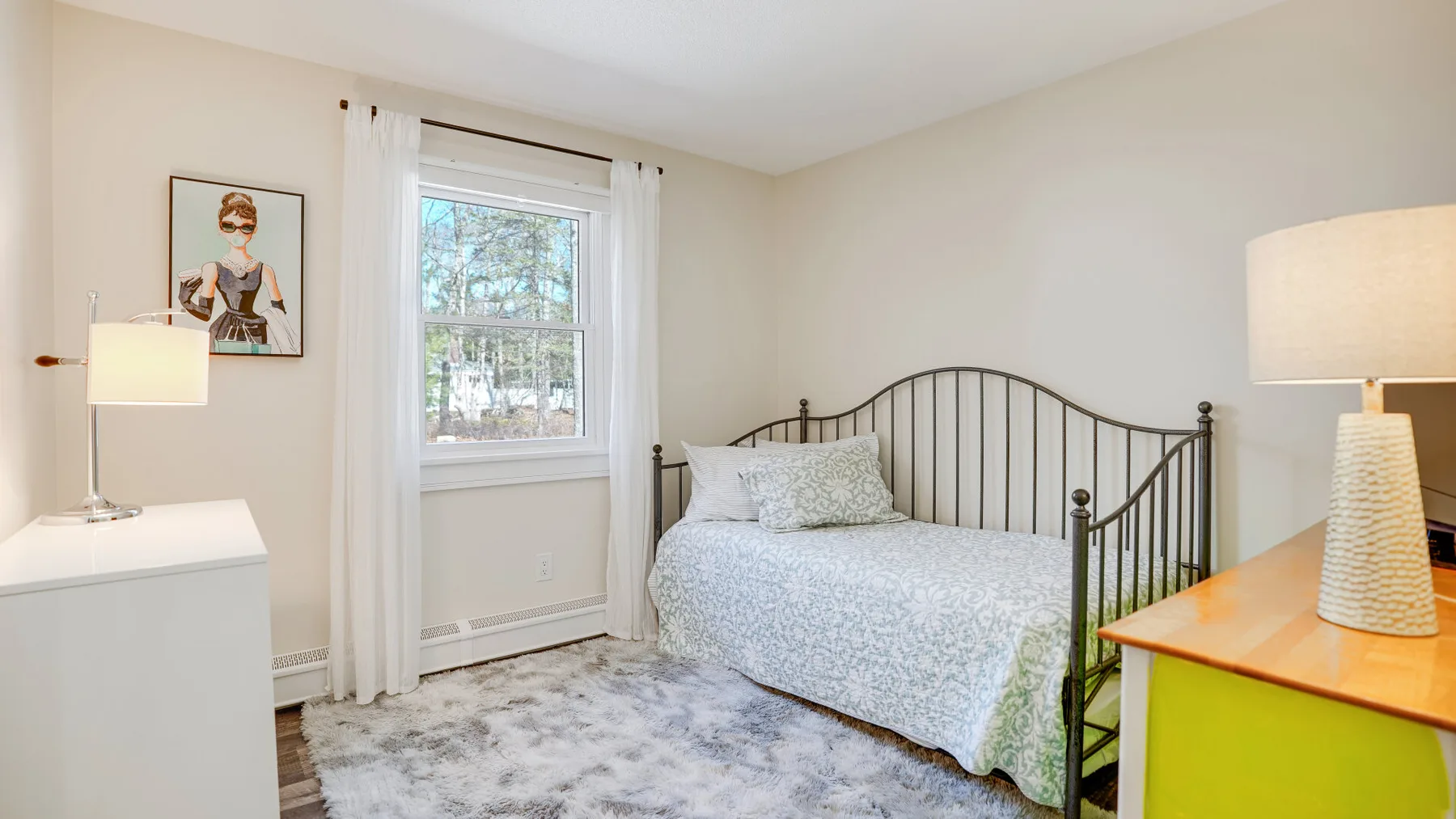 A bedroom with a metal bed beneath a window and light-colored bedding.