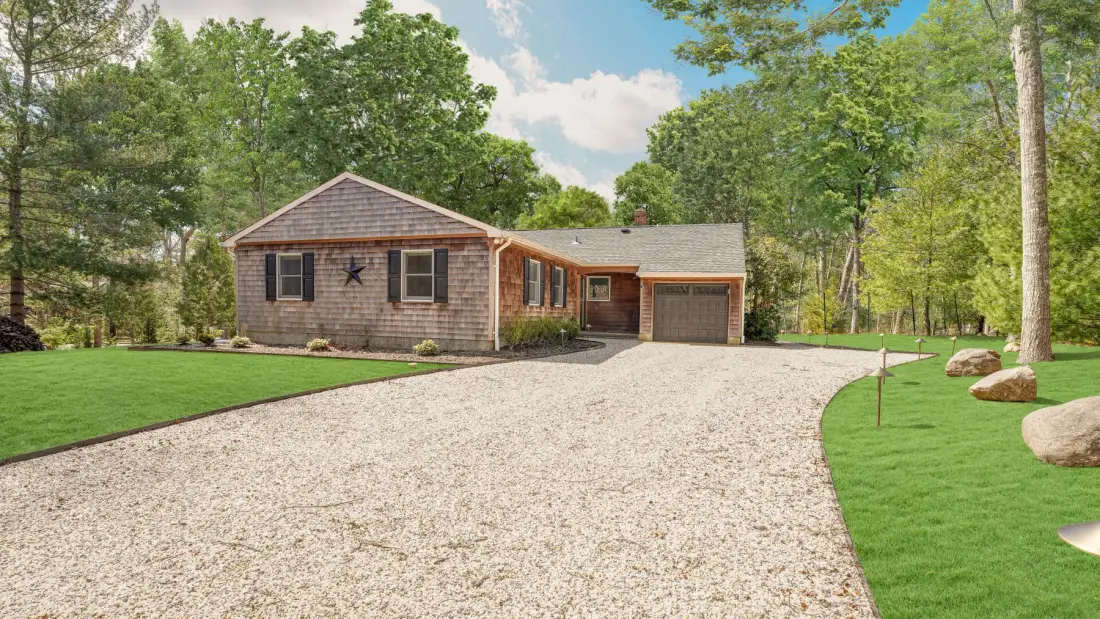 A house with a gravel driveway, lawn, and trees.