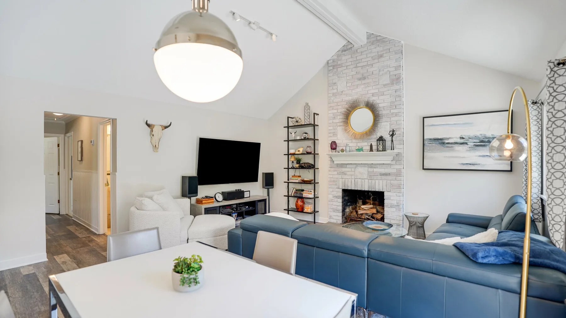 A bright living room with blue seating, a television, and a brick fireplace.