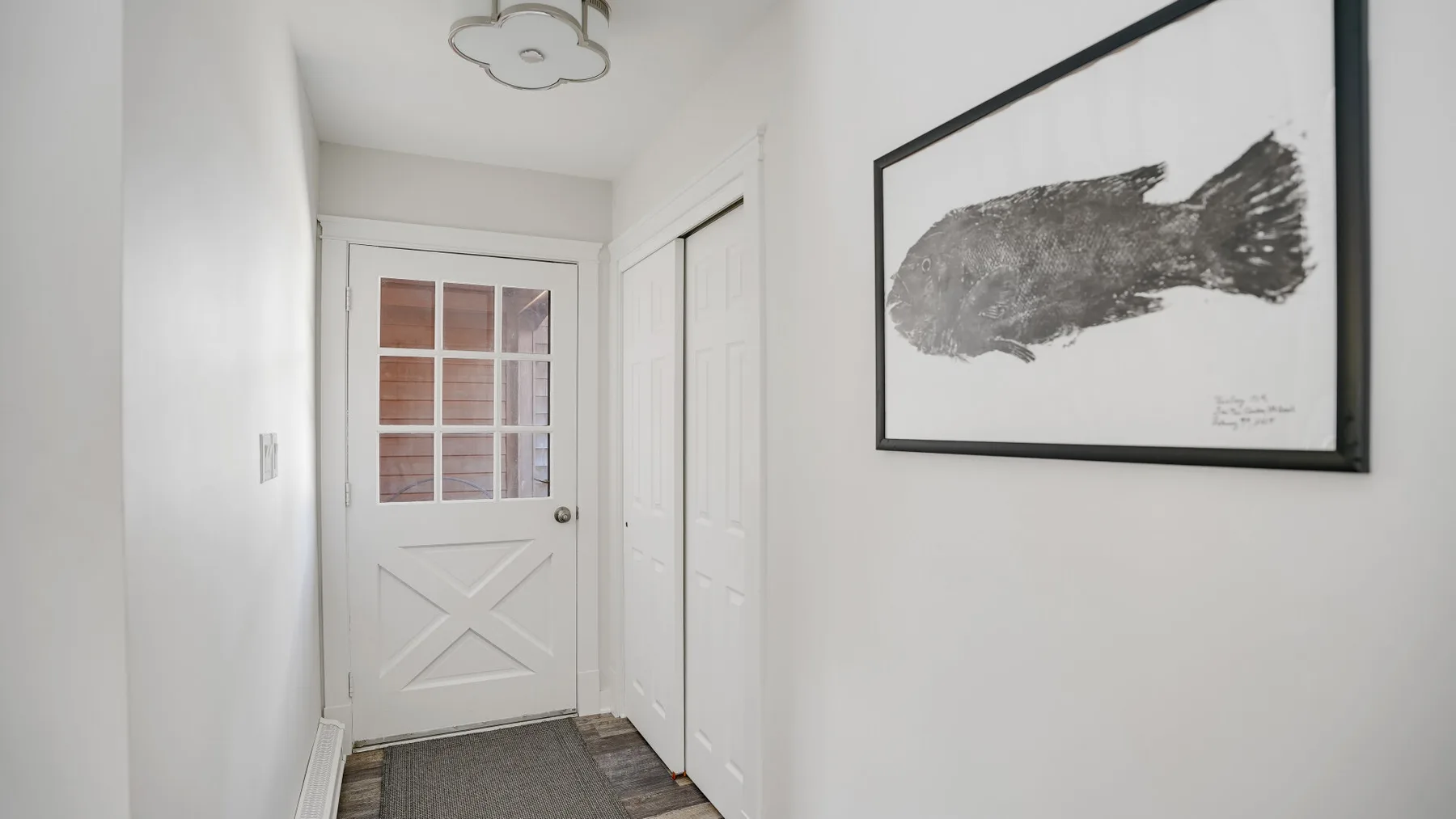 A bright entry hallway with a white door and framed fish artwork.