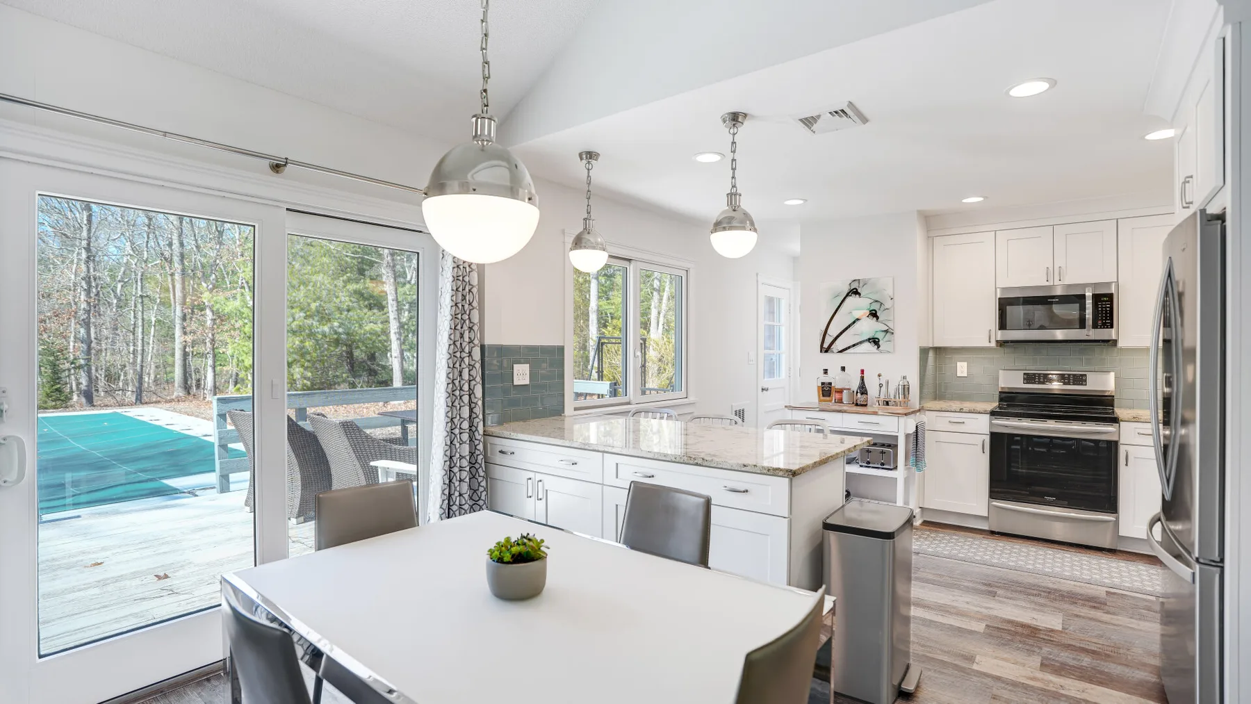 A bright kitchen and dining area opens onto a deck beside a swimming pool.