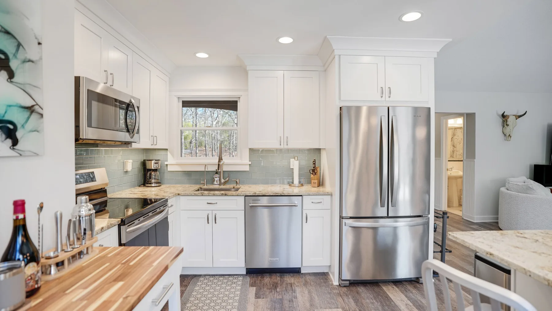 A bright kitchen with white cabinets, stainless steel appliances, and a window above the sink.
