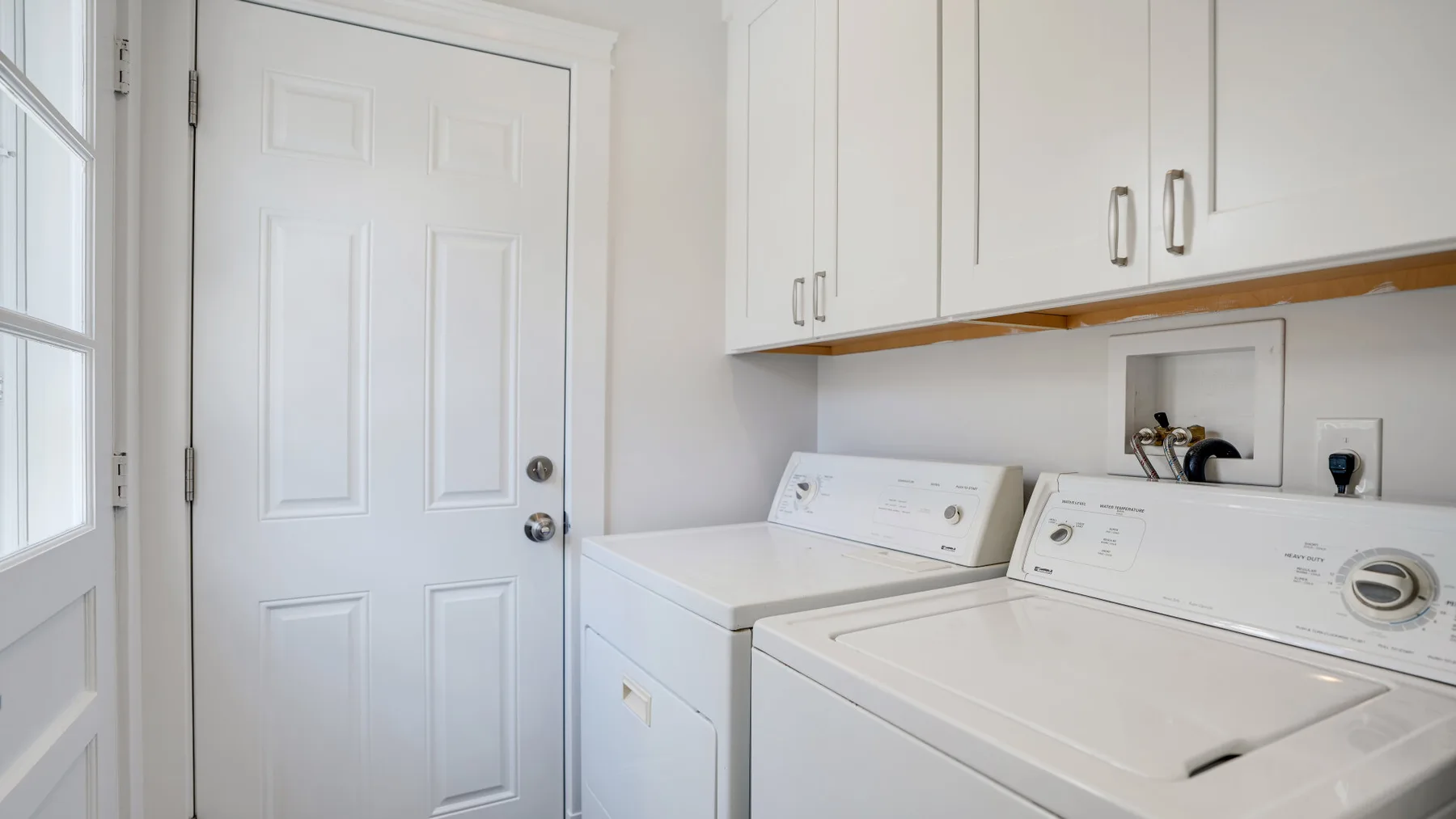 A laundry room with a washer and dryer beneath white cabinets.
