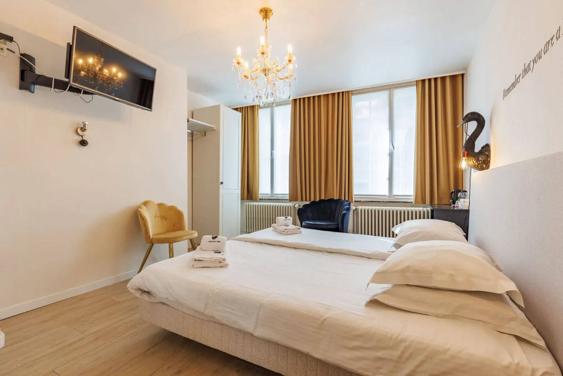 Habitación de hotel con ropa de cama blanca, una lámpara de araña de cristal, cortinas doradas y una silla decorativa amarilla.