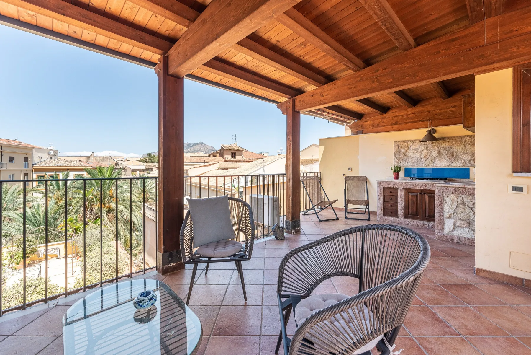 Una terraza cubierta con asientos al aire libre da a edificios cercanos y palmeras.