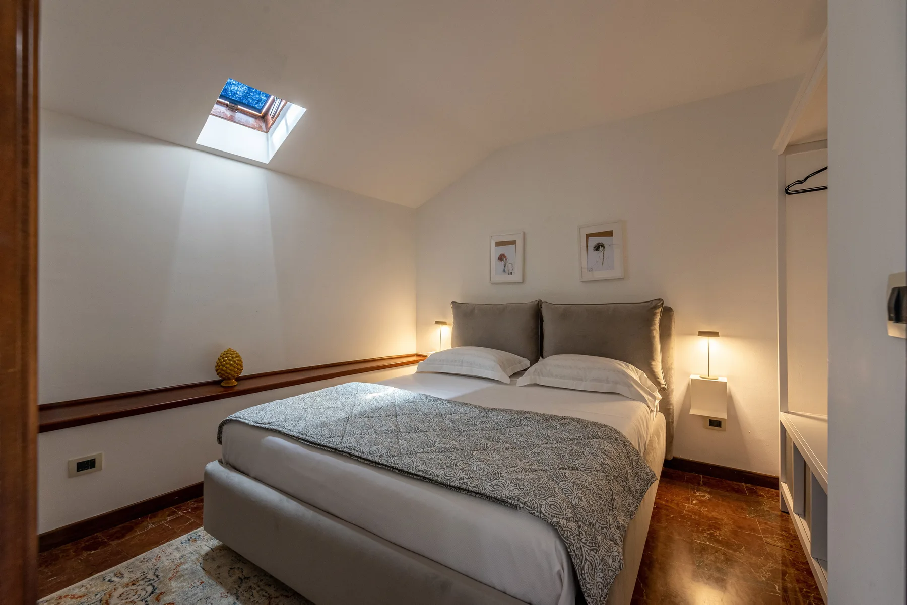 Un dormitorio con una cama bajo un techo inclinado y una claraboya.