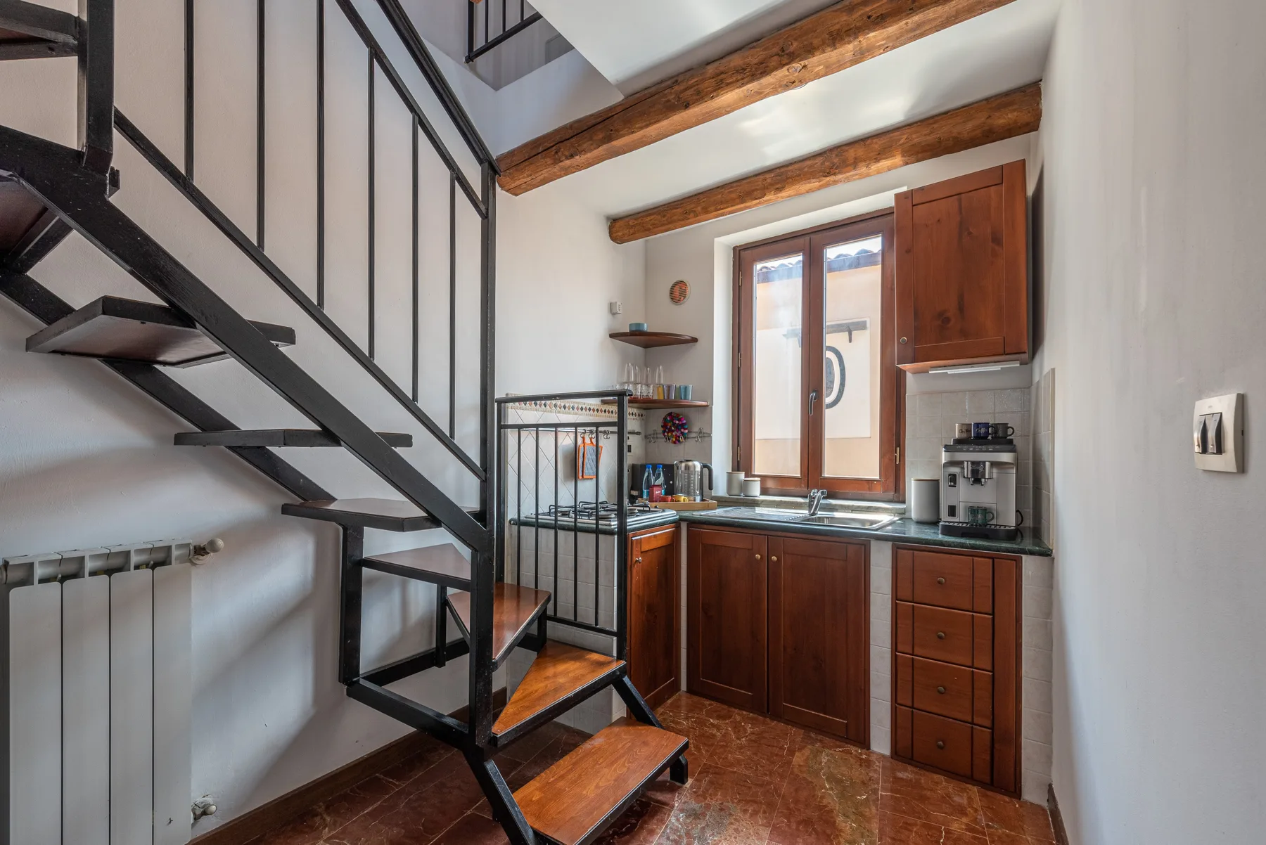 Una cocina compacta con ventana, armarios de madera y una escalera metálica.