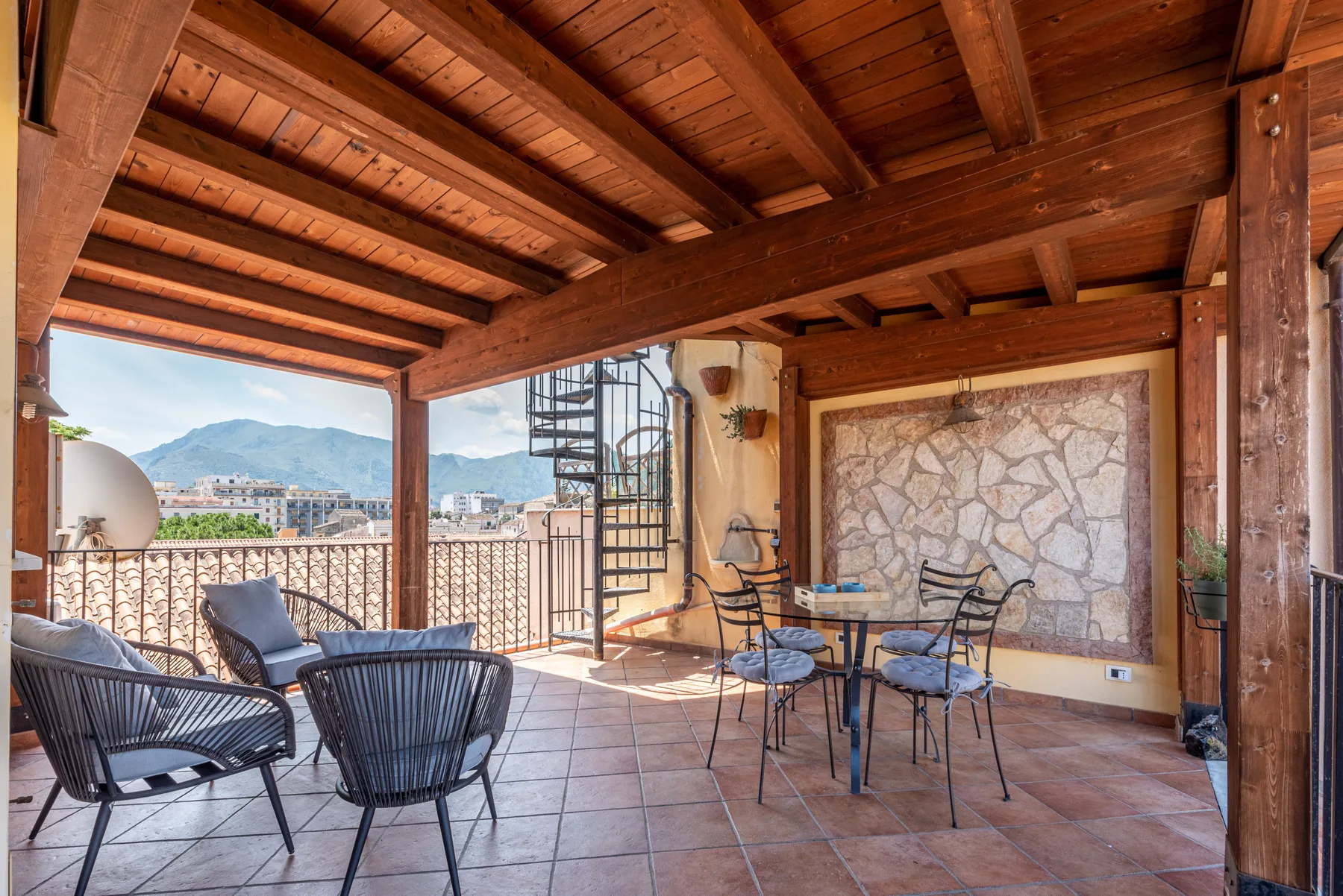 Una terraza exterior cubierta tiene asientos y una mesa con vistas al paisaje circundante.