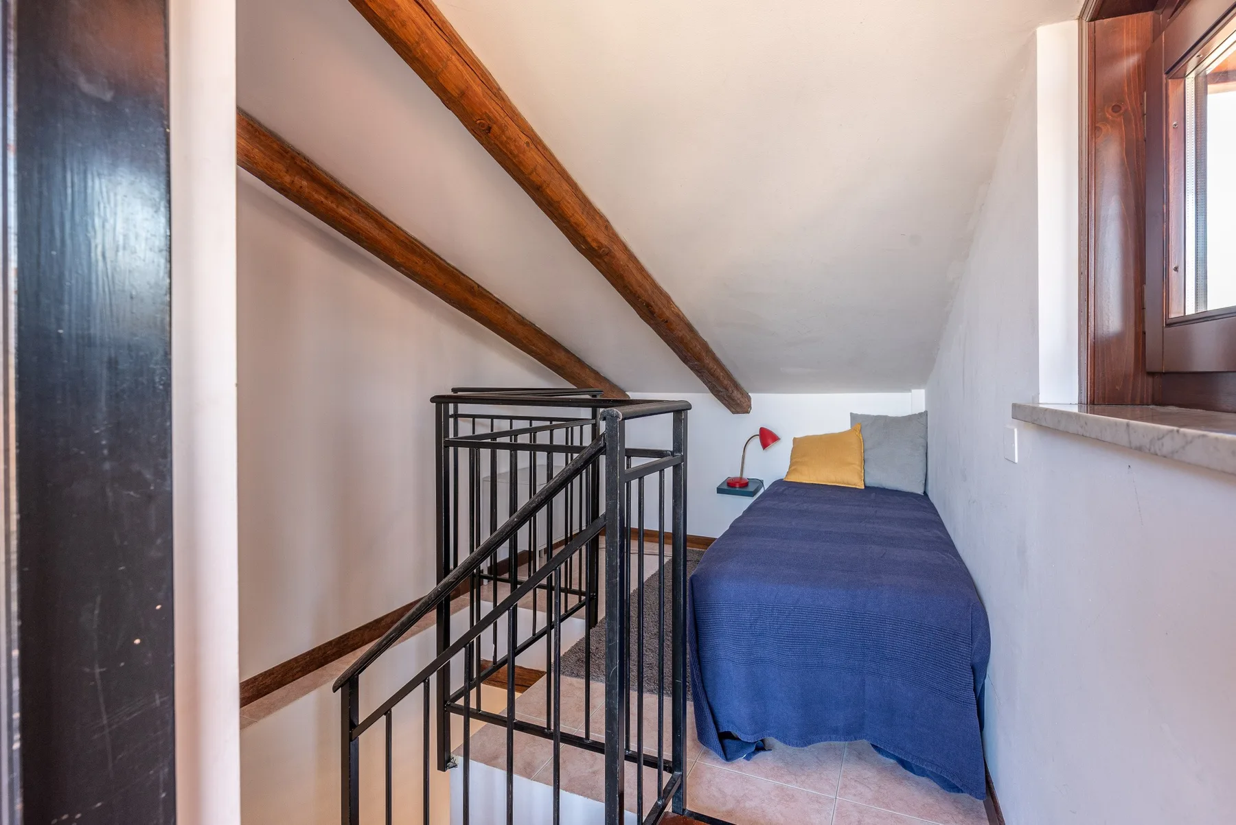 Una estrecha zona para dormir con una cama bajo vigas de madera expuestas.