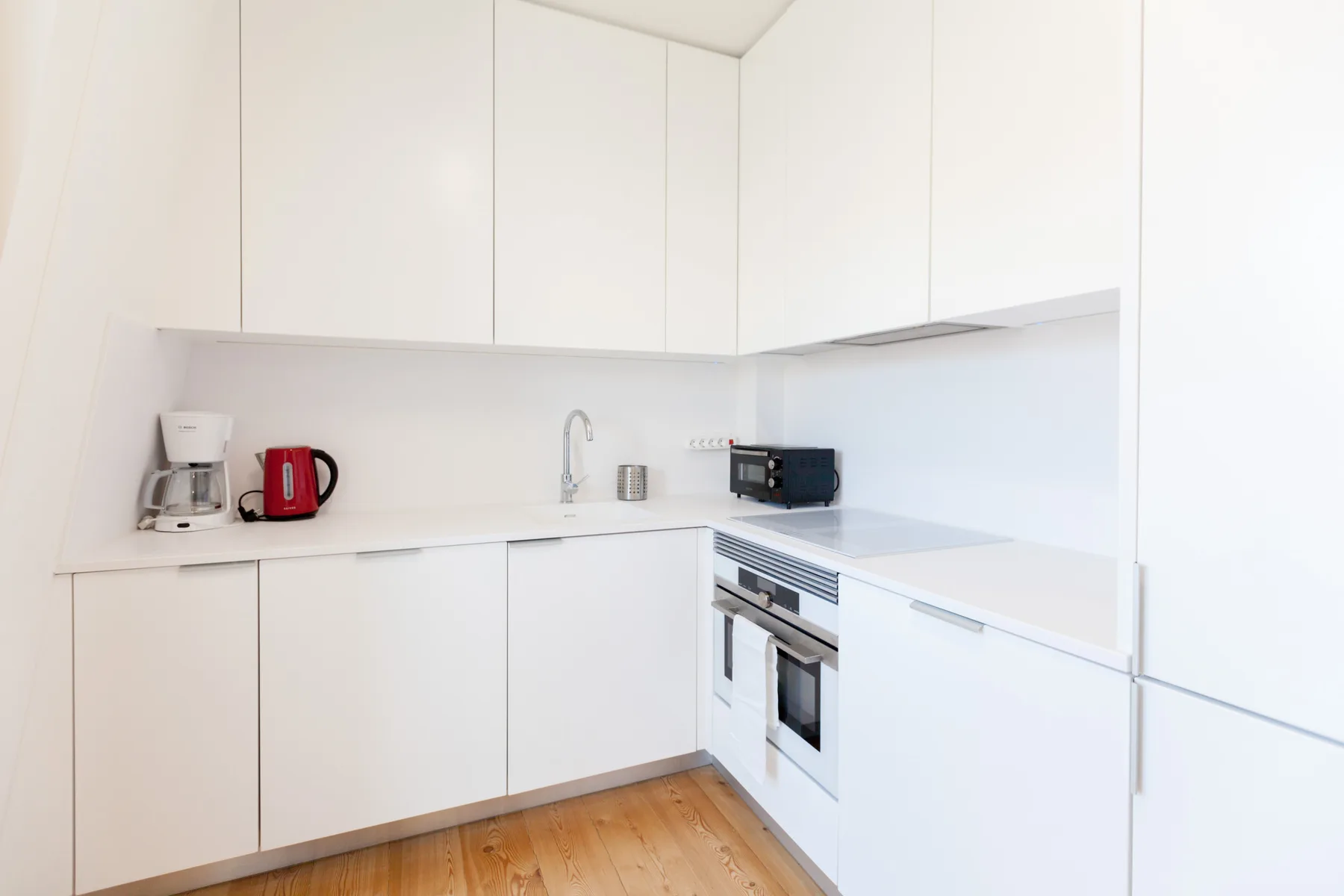 Una cocina blanca y luminosa con electrodomésticos integrados y suelo de madera.