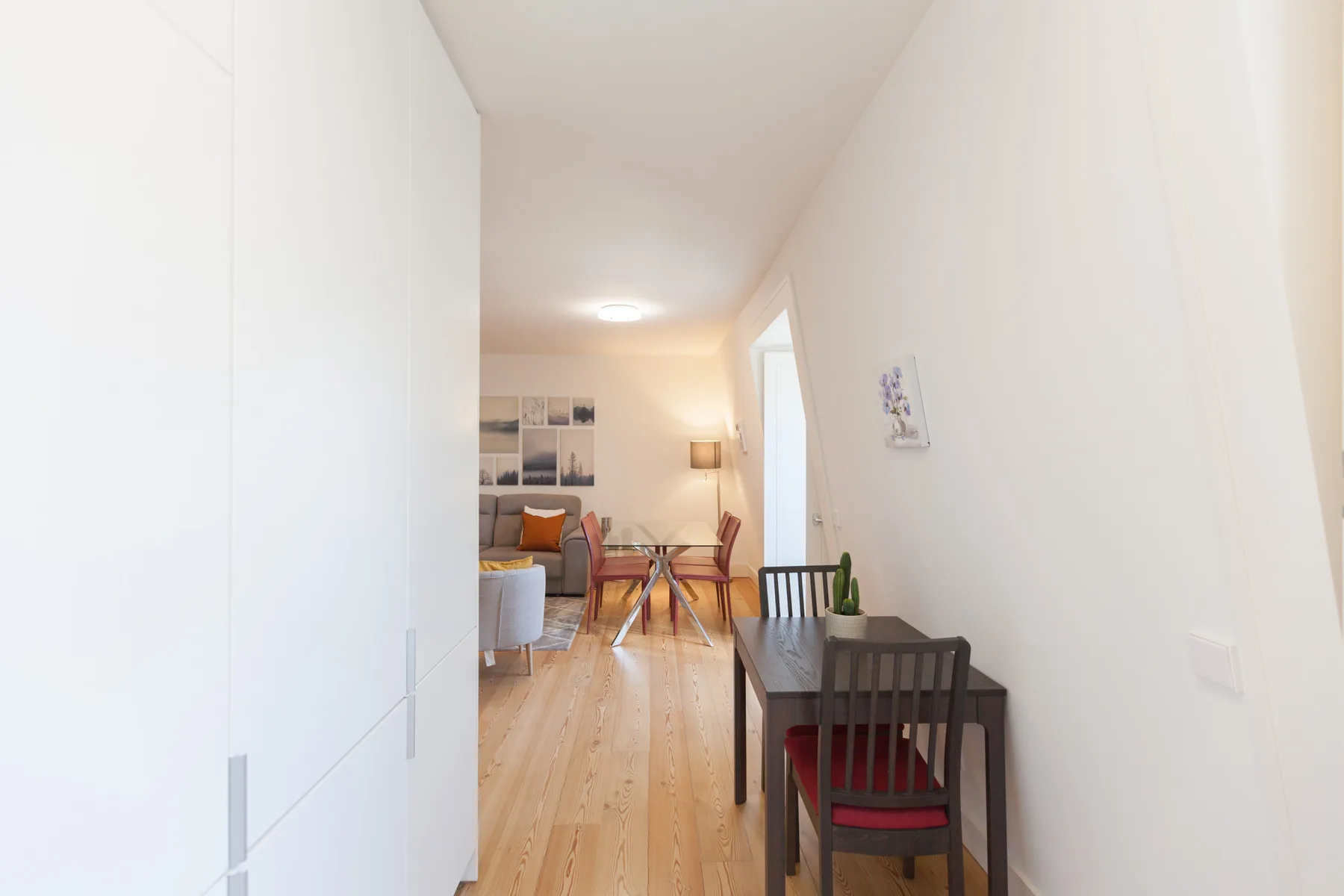 Un pasillo estrecho da a una luminosa sala de estar y comedor con suelo de madera.
