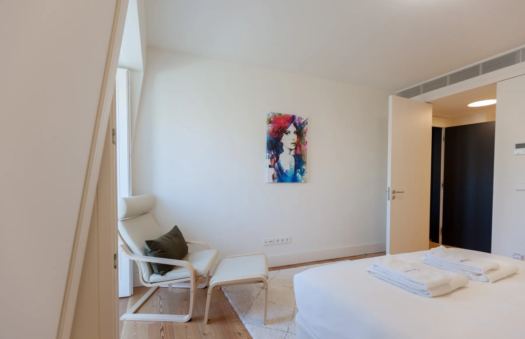 Un dormitorio luminoso con una cama, una zona de estar y arte colorido en la pared.