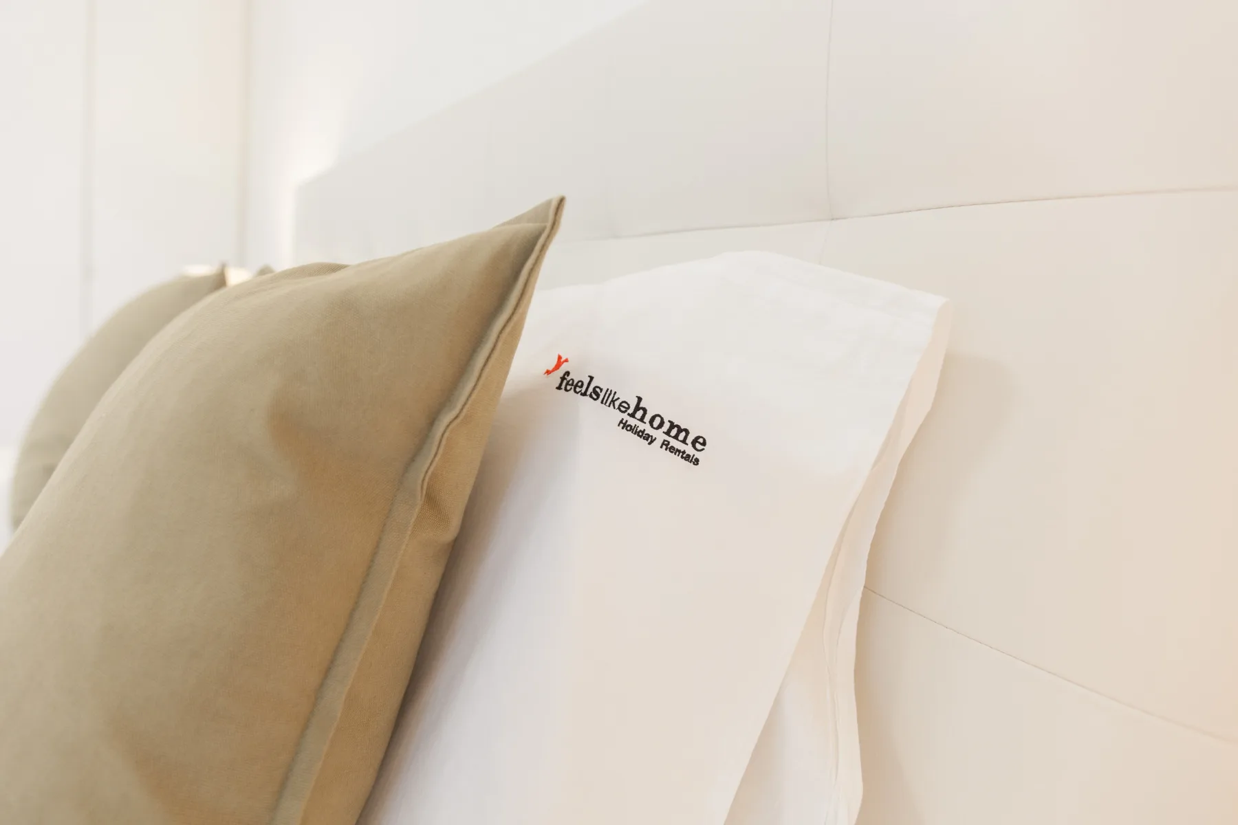 Primer plano de una cama con un cojín beige y otro blanco con una marca.