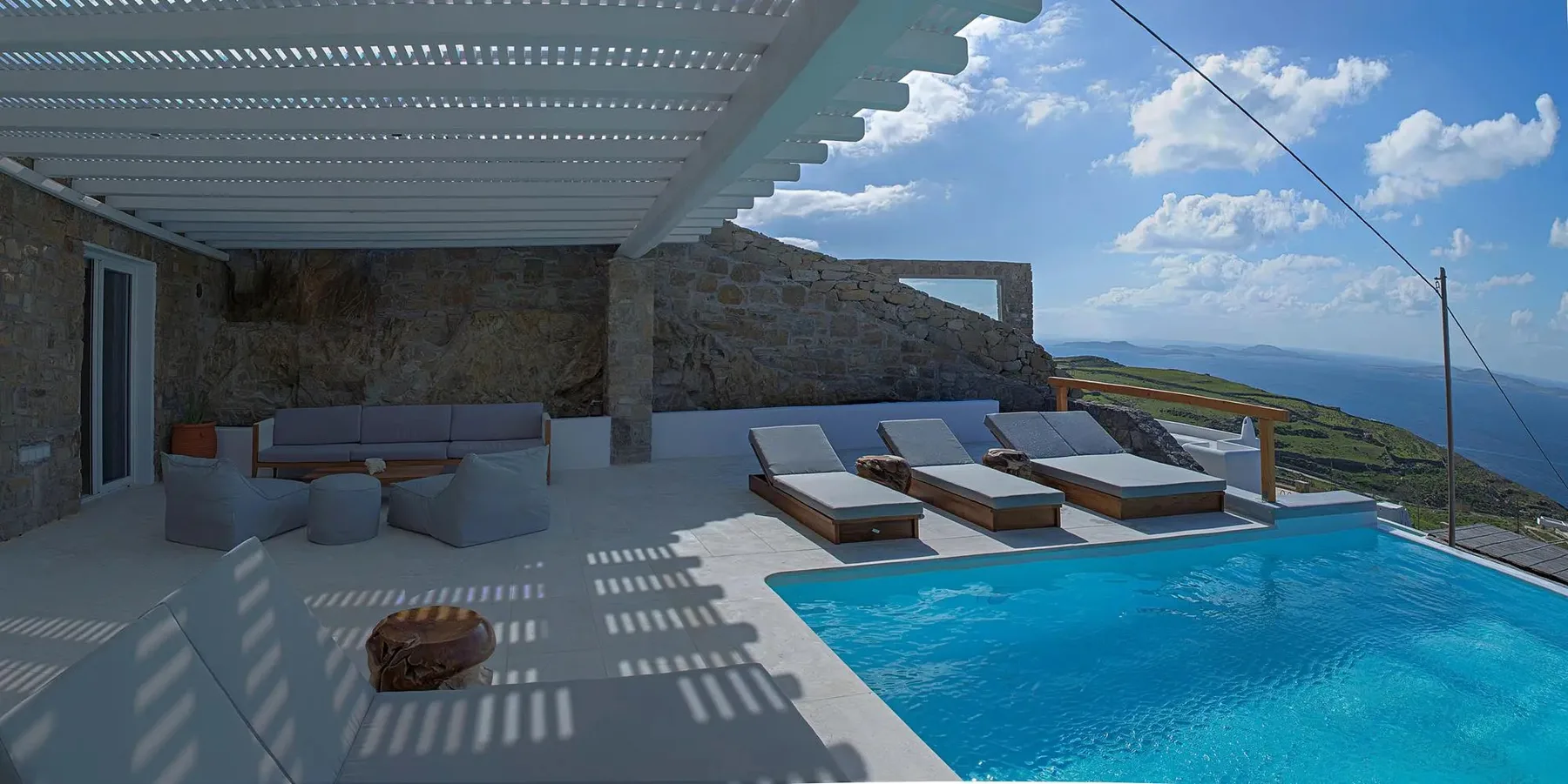 A shaded outdoor seating area beside a swimming pool overlooks the sea.