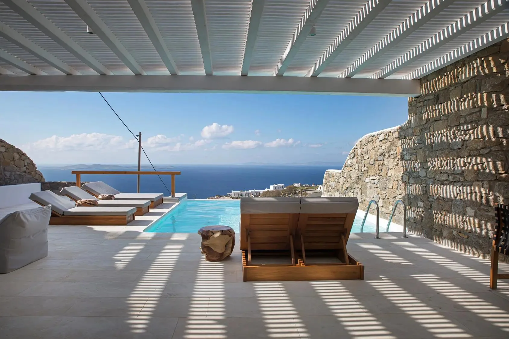 A shaded pool terrace overlooks the sea, with lounge seating beneath a slatted canopy.