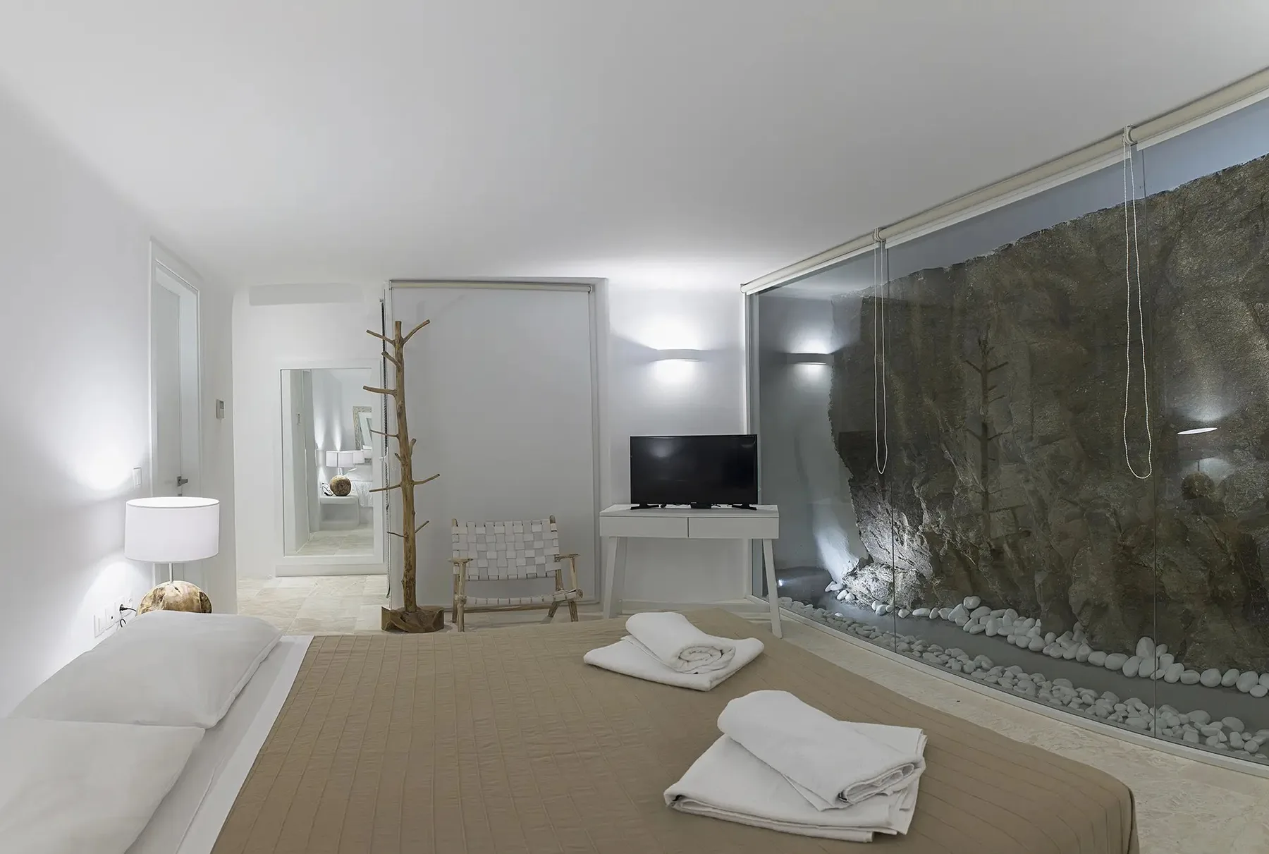 A modern bedroom with a bed, television, and a glass wall overlooking a rock feature.