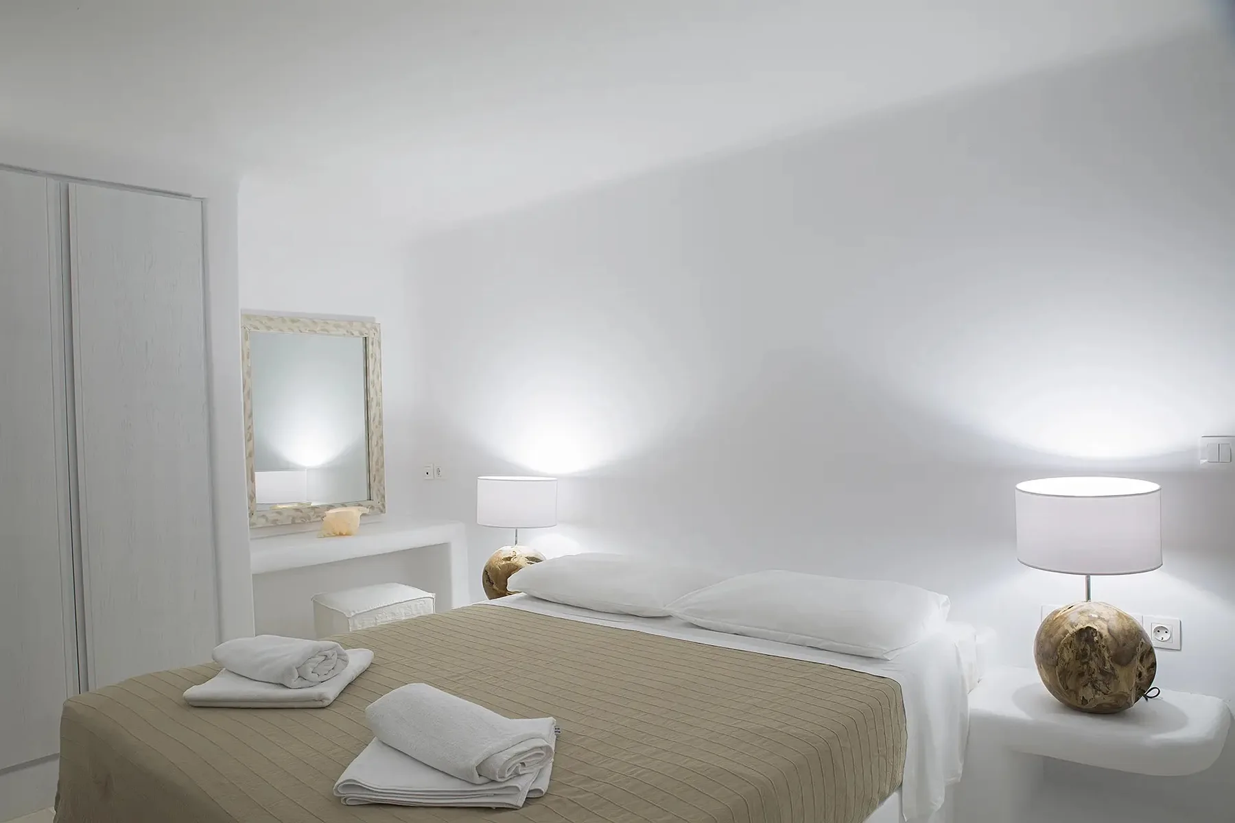A bedroom with a neatly made bed, folded towels, and a bedside lamp.