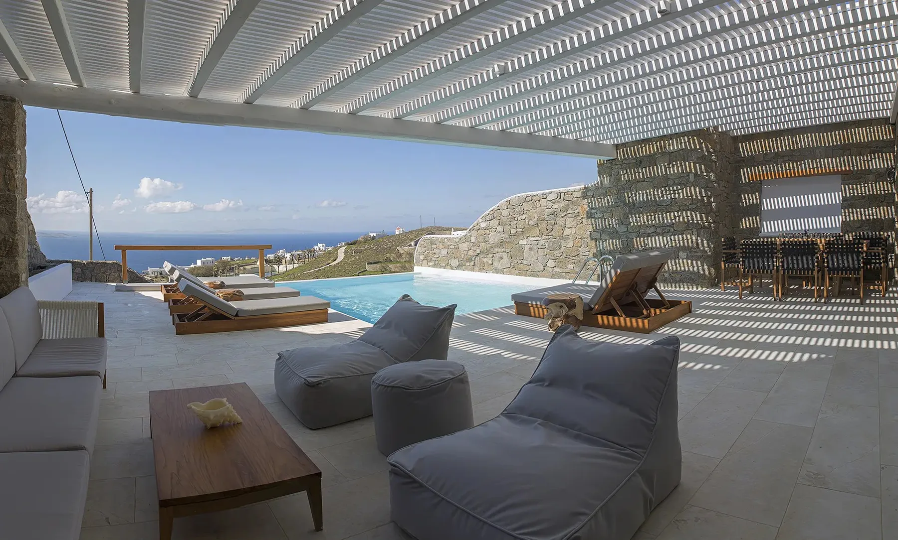 A shaded outdoor lounge opens onto a pool and a sea view.