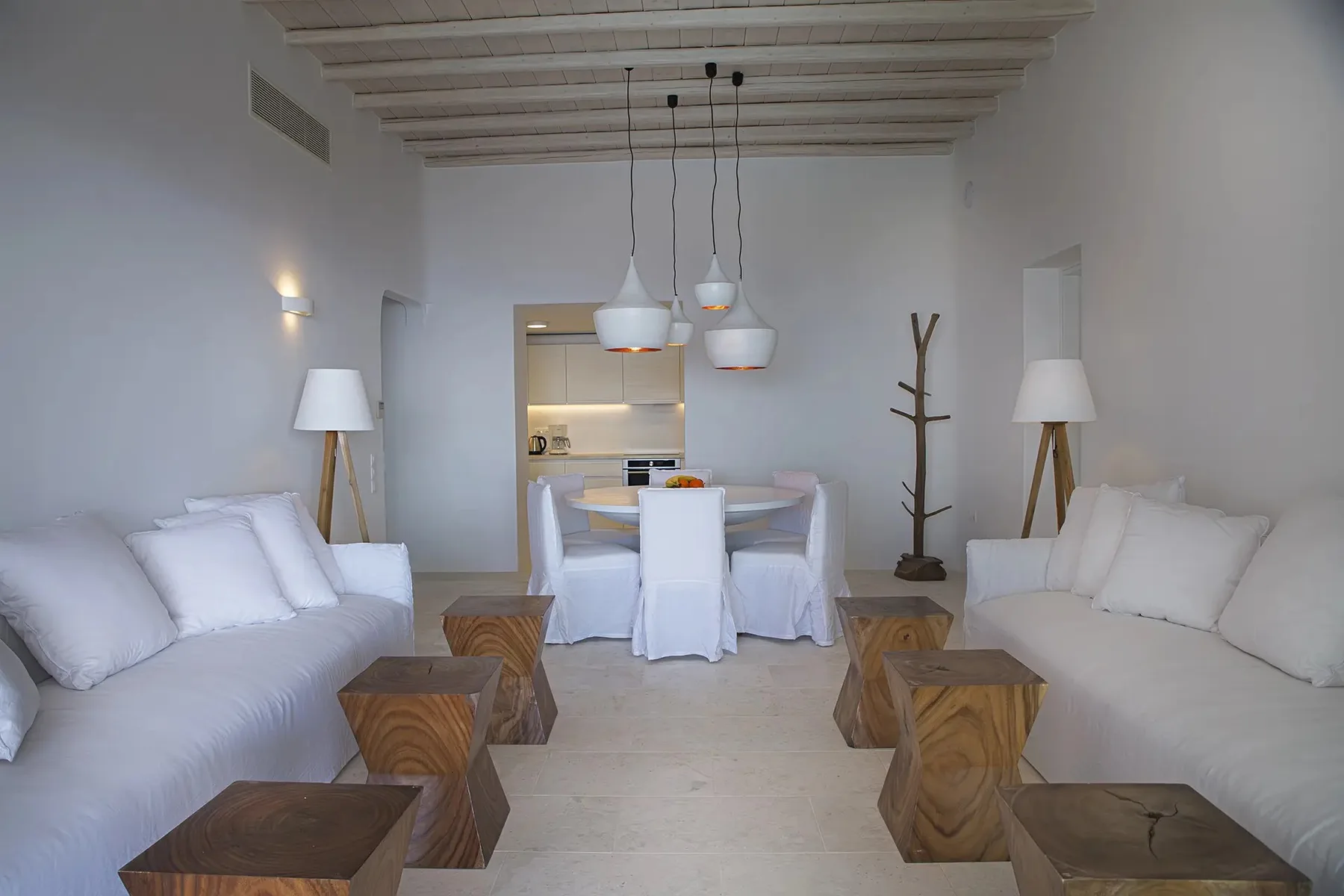 A bright living room with white seating and a dining table beneath pendant lights.