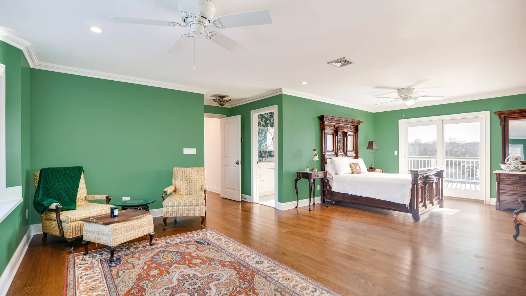 Un dormitorio con paredes verdes tiene una cama grande, asientos y una alfombra estampada.