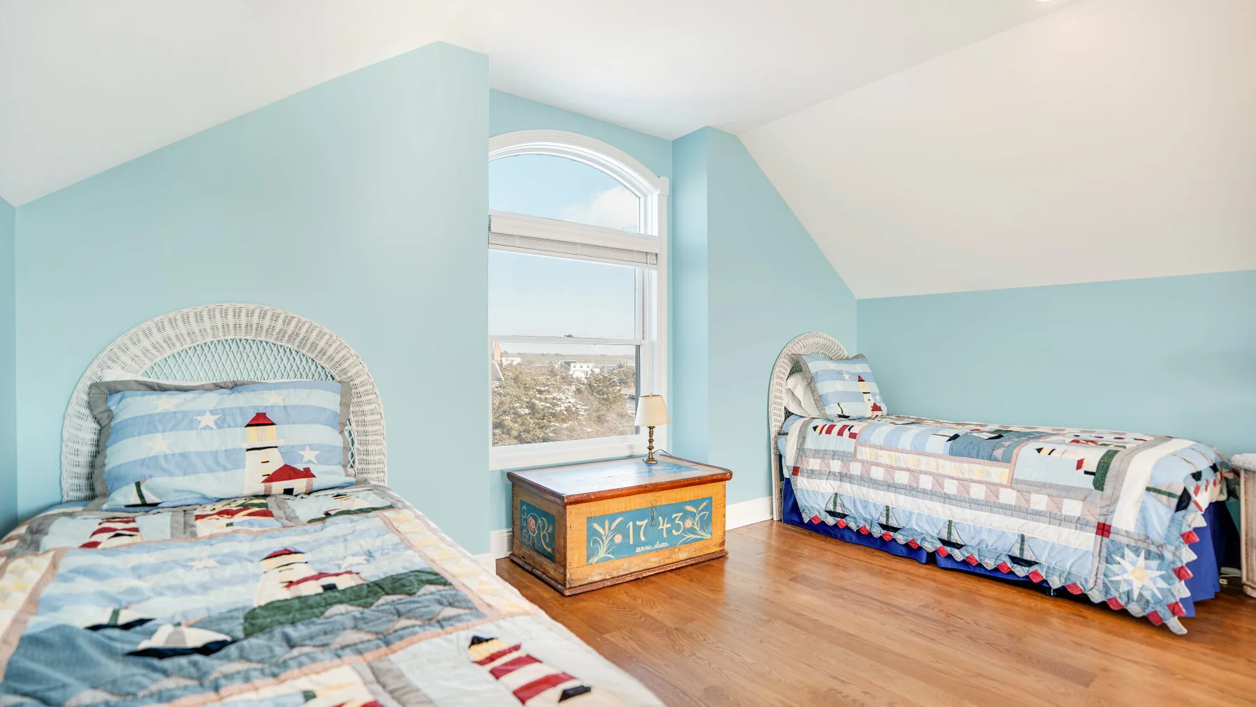 Un dormitorio luminoso con dos camas y un baúl de madera colorido entre ellas.