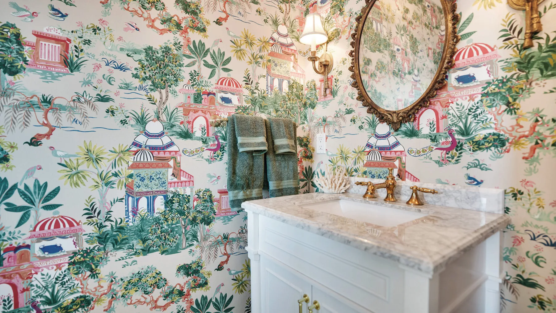 Un tocador de baño con encimera de mármol está frente a un papel tapiz floral colorido.