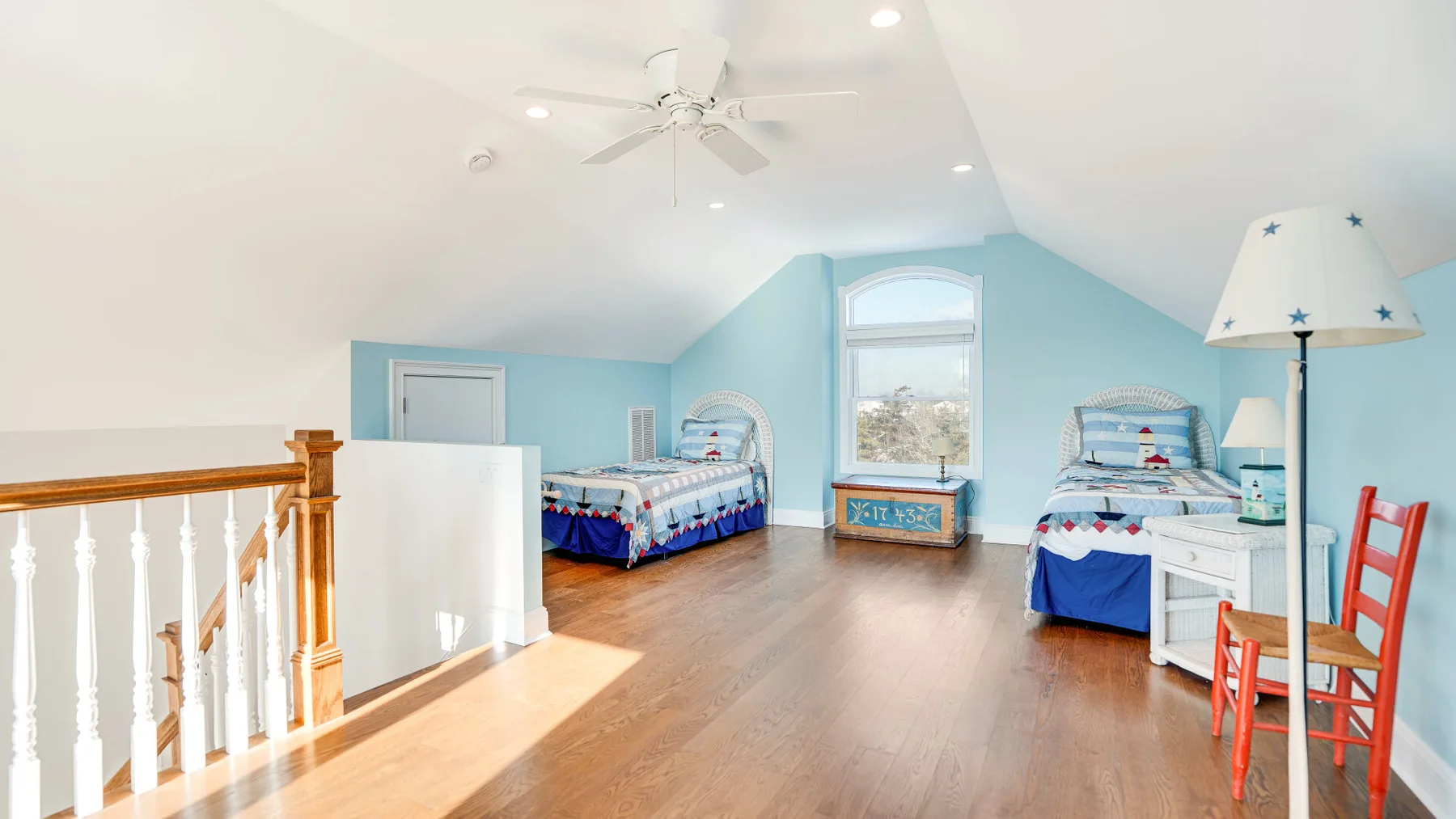 Un dormitorio luminoso con dos camas, una ventana y suelo de madera.