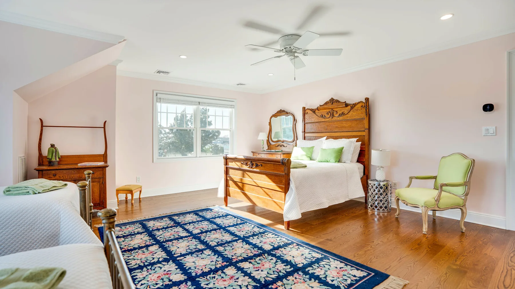 Un dormitorio luminoso con una cama grande, una ventana y una alfombra estampada.