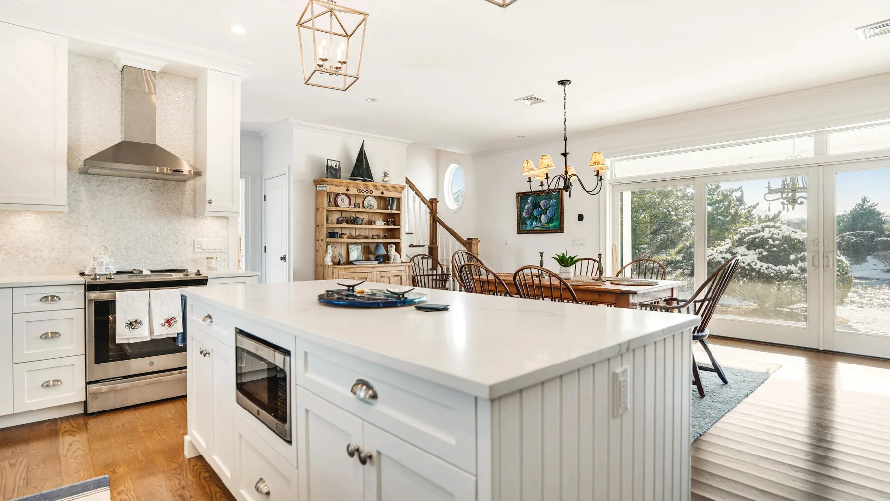 Una cocina luminosa con una gran isla blanca y comedor junto a amplias ventanas.