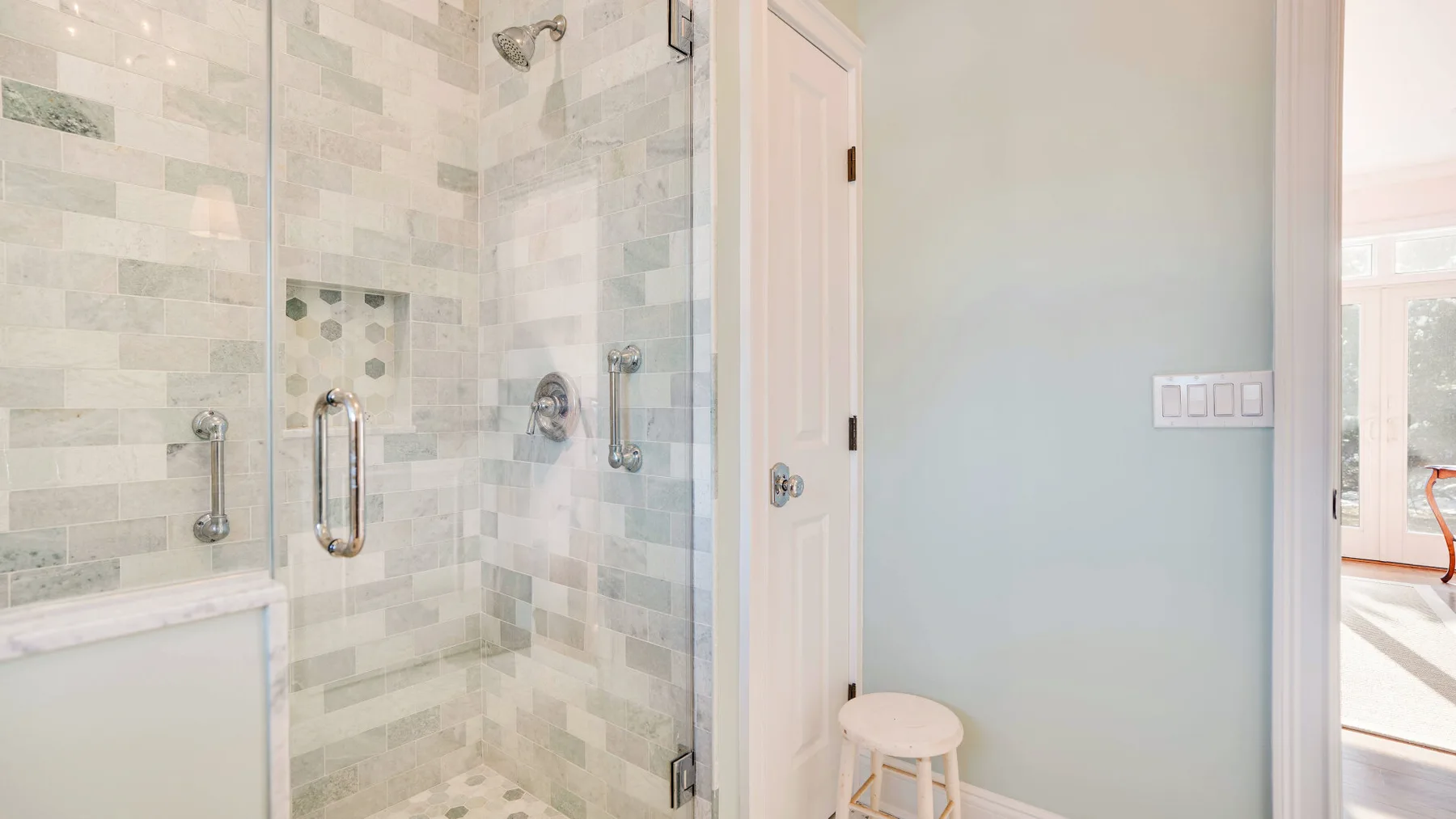 Un baño luminoso con una ducha de azulejos y un pequeño taburete junto a la puerta.