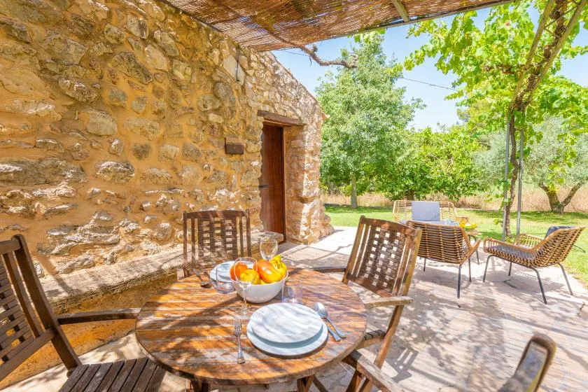 A shaded outdoor dining area beside a stone wall, with a table and chairs.