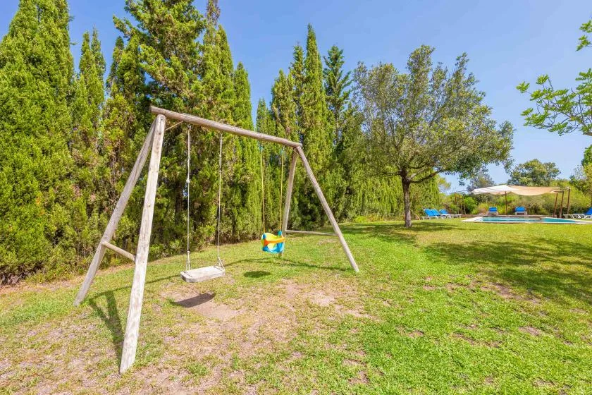 A grassy outdoor yard has a wooden swing set beneath tall trees.
