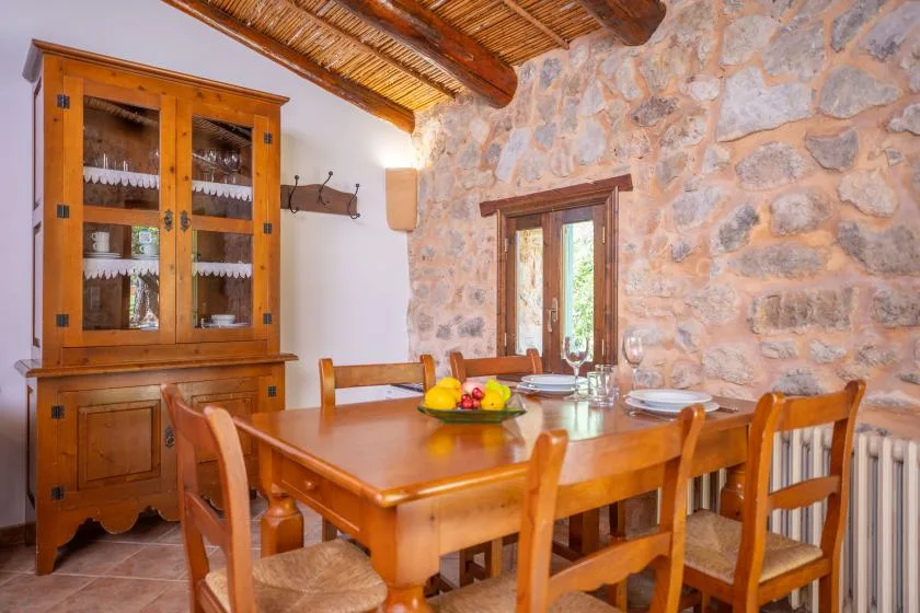 A dining room with a wooden table and chairs beside a stone wall.
