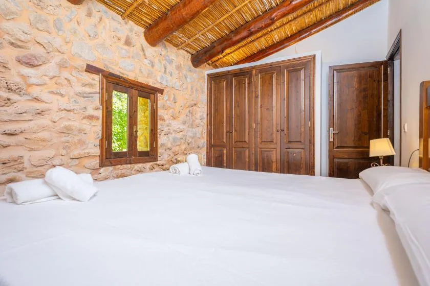 A bedroom with a large bed, stone wall, and wooden ceiling beams.