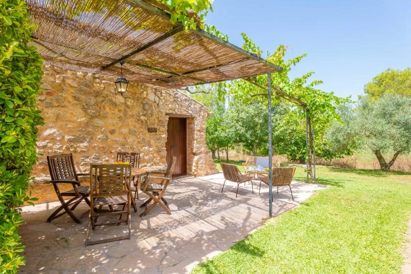A stone patio with outdoor seating sits beneath a vine-covered pergola.