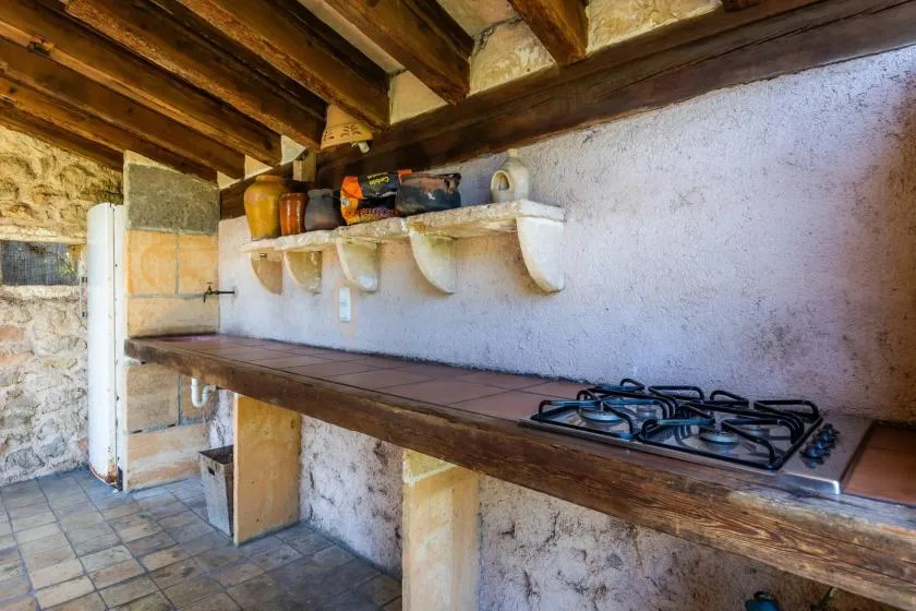 A rustic kitchen with a long counter and a gas cooktop beneath wooden ceiling beams.
