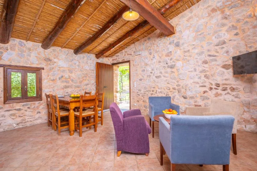 A stone-walled living and dining room with wooden seating and a tiled floor.