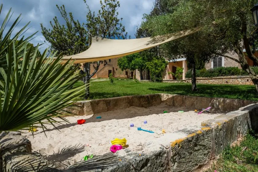 A sandy play area sits beneath a shade sail in a grassy garden.