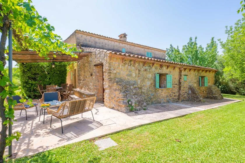 A stone house with a shaded outdoor seating area beside a green lawn.