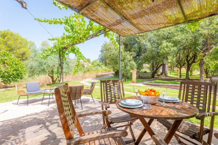 An outdoor dining area sits beneath a woven shade canopy, with trees beyond.