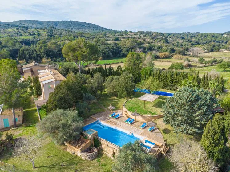 An outdoor swimming pool sits among landscaped grounds with wooded hills in the distance.