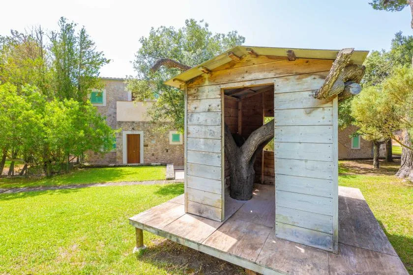 A small wooden shed stands on a raised platform in a grassy, tree-lined yard.