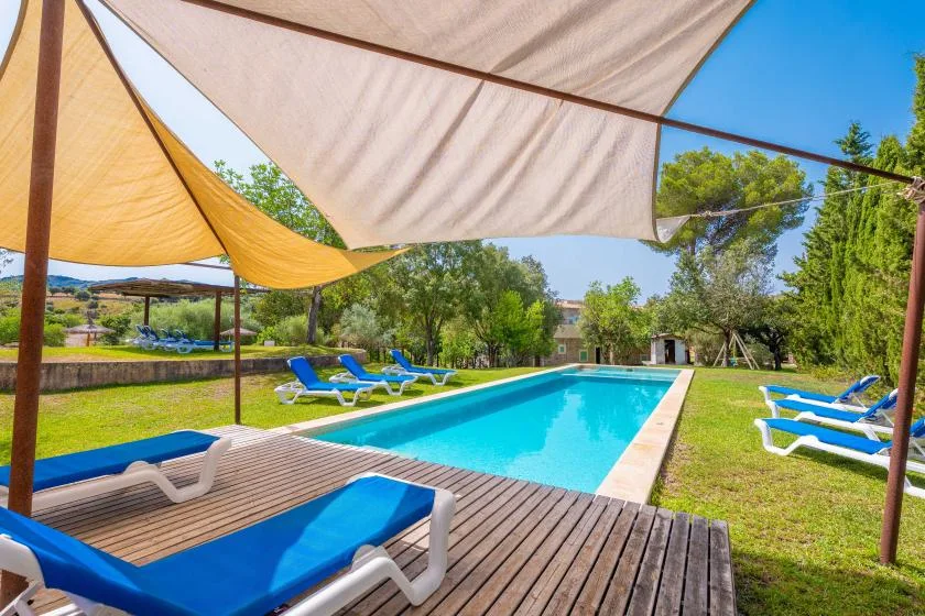 An outdoor swimming pool sits beside a wooden deck and shaded lounge seating.