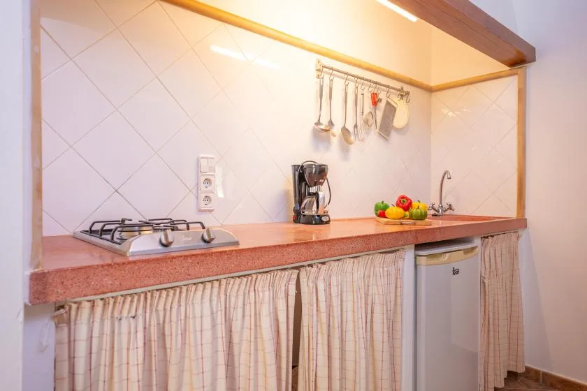A compact kitchen counter with a stovetop, coffee maker, and hanging utensils.