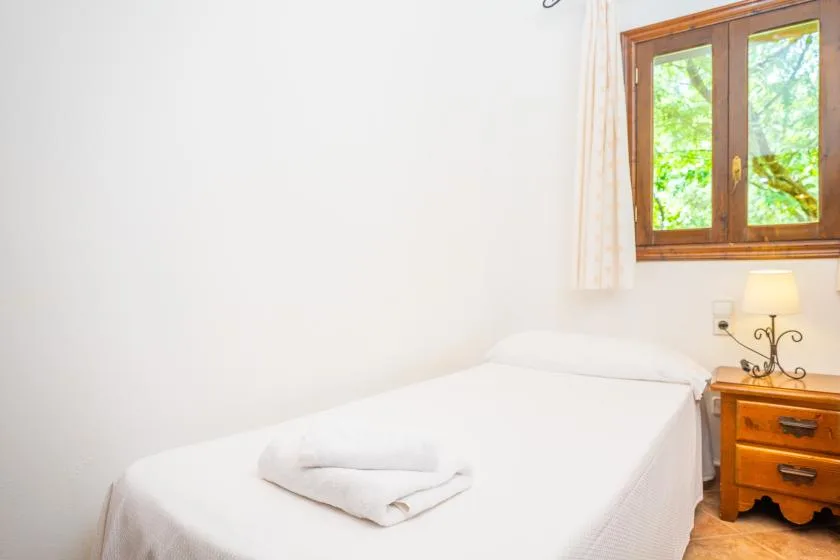 A bright bedroom with a neatly made bed beneath a wooden-framed window.