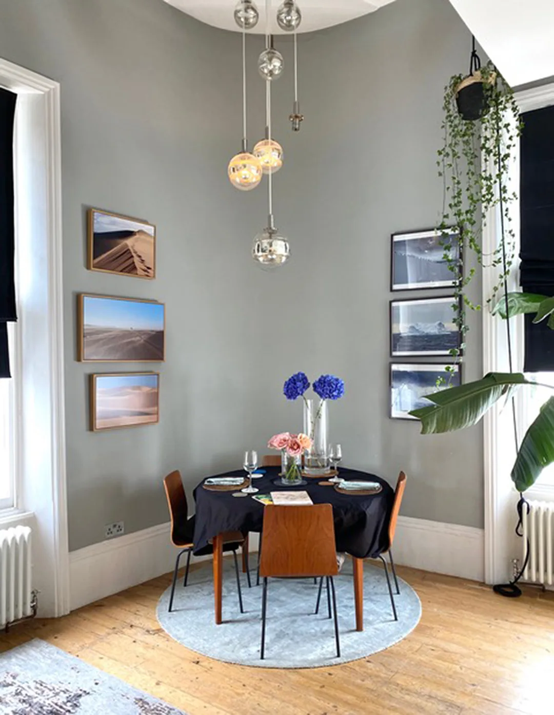 A dining area with a round table set beneath hanging lights and framed pictures.