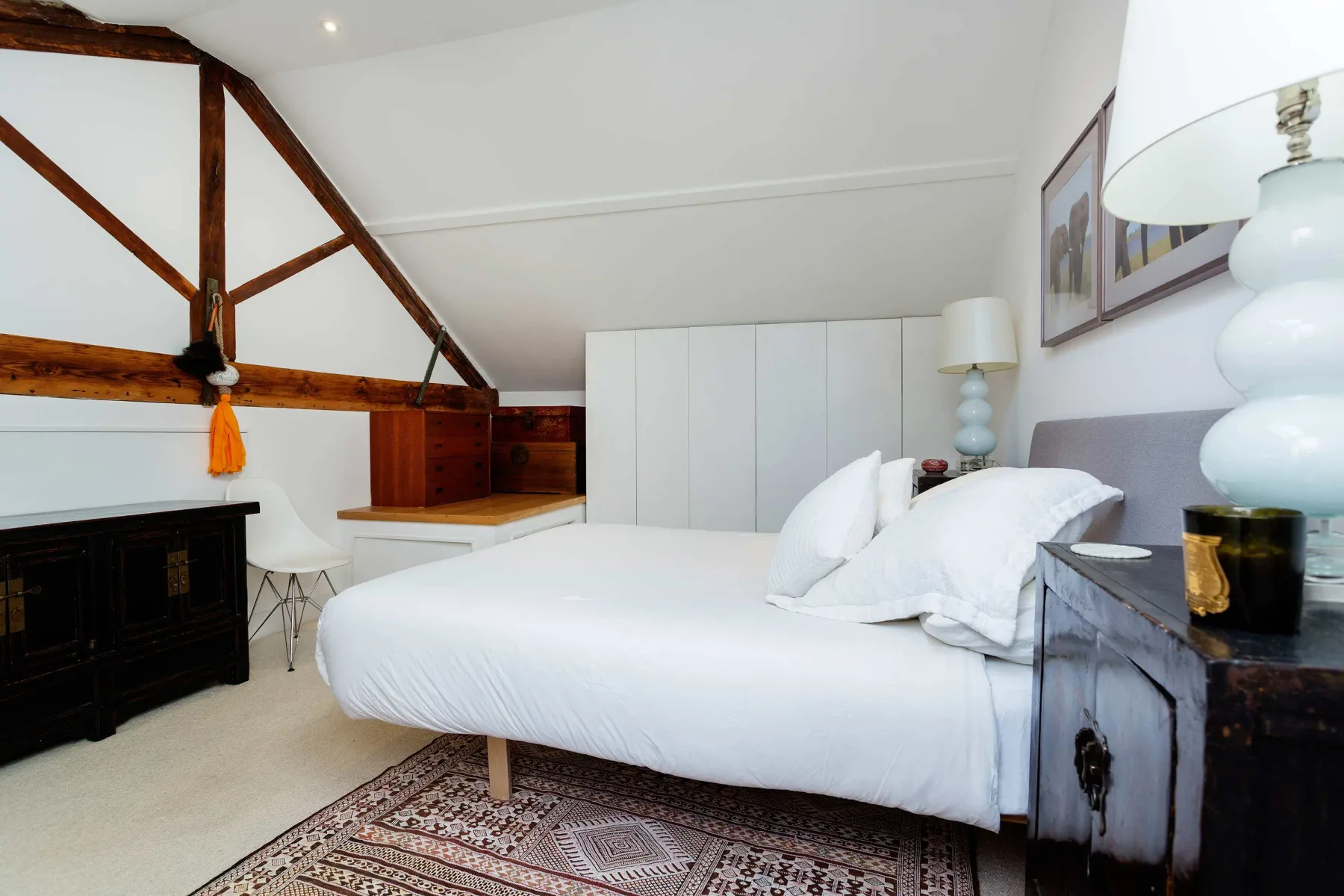A bright bedroom with a large bed, framed artwork, and exposed wooden beams.