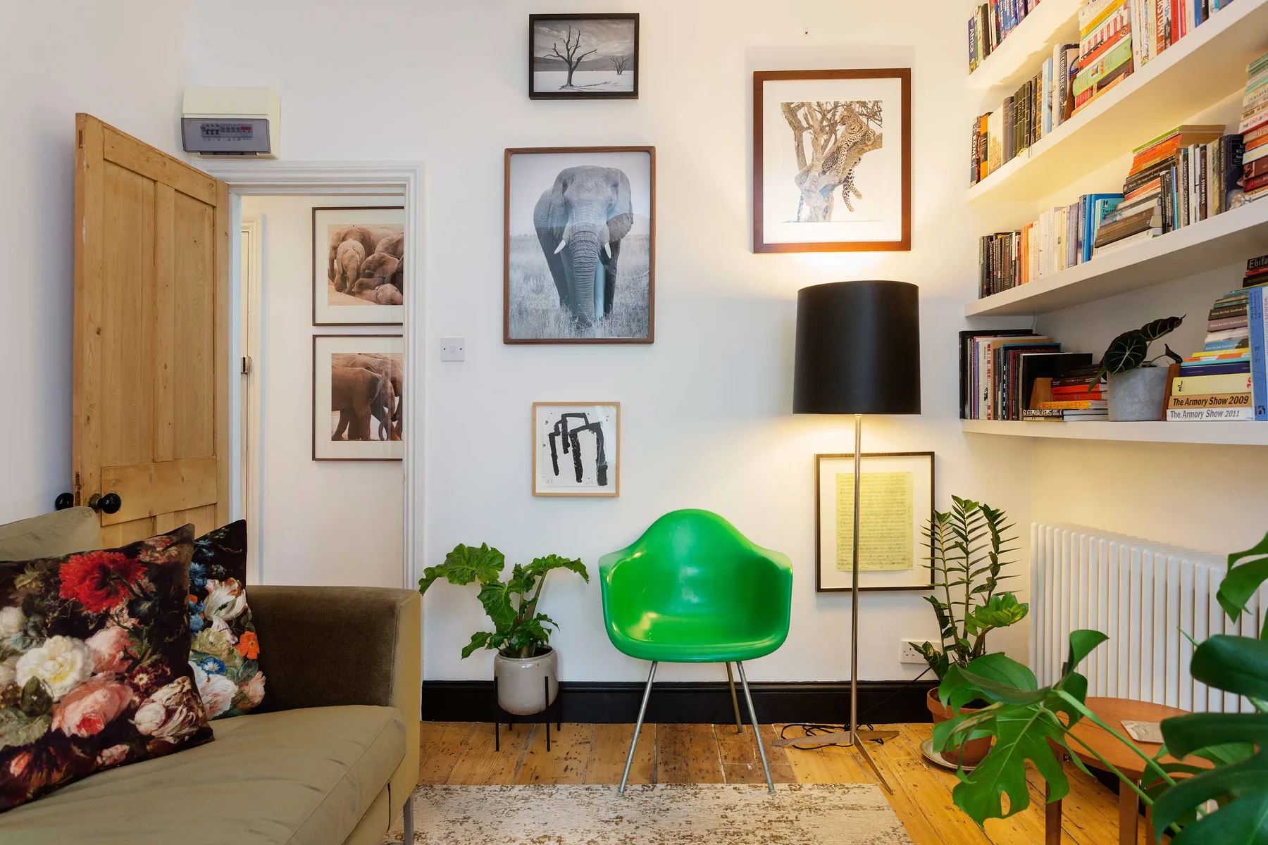 A living room with a green chair, wall art, and bookshelves.
